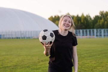 Portrait of female football player holding ball on the soccer field at sunset