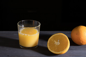 a glass of freshly squeezed orange juice and oranges on a dark background