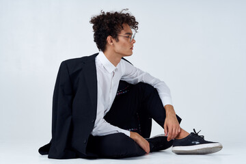 stylish man with curly hair in sneakers on a light background a jacket on the shoulder pants model