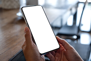 Mockup image of a woman holding mobile phone with blank white desktop screen