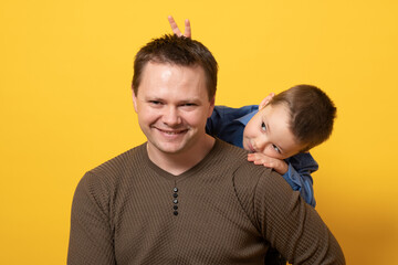 Happy father's day! Cute father and son hugging on yellow background. Portrait of a dad with a baby boy smiling and hugging. Family concept.