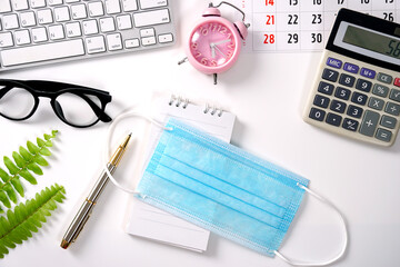 White Office Desk with medical mask Computer Notepad pencil Green leaf and other Supplies. Blank...
