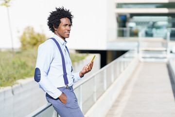 Black man with afro hairstyle using a smartphone near an office building.