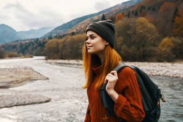 woman in a sweater cap with a backpack on her back mountain river in nature