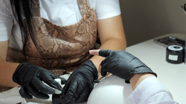 A manicure master in black gloves and a protective mask gives a manicure to a girl. Close-up of a cosmetologist's hand filing a woman's nails in a beauty salon. The concept of health and beauty