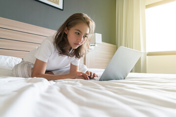 Asian woman lying down and smiling the bed and laptop