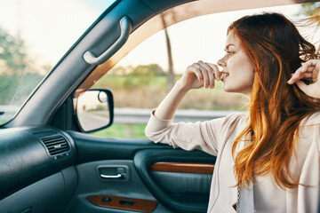 Fototapeta na wymiar happy woman with red hair in front seat of car touching face with hands cropped view