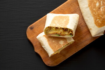 Homemade Breakfast Egg Burrito with Avocado and Bacon on a rustic wooden board on a black background, top view. Flat lay, overhead, from above. Space for text.