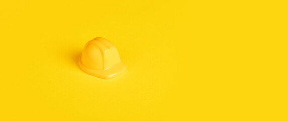 Yellow toy worker's helmet over yellow background, minimalism construction concept, panoramic image