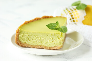 Piece of lemon cheesecake with mint on a white plate