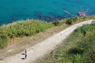 A young couple walks along a dirt road to reach a small beach on the Abruzzo coast. Trabocchi coast, Abruzzo, Italy