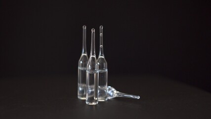 Glass transparent ampoules. Transparent liquid. Medicine. Vaccine against the virus. Medical drug. Solution for injections. Black background. Close-up.