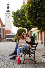 Fototapeta na wymiar Beautiful young couple cuddling on a bench in a European town. Romatnic date and love concept.