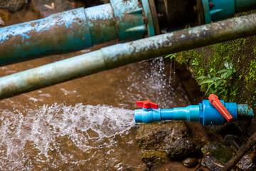 Blue water pipe with orange water opener, water gushing out of the PVC pipe. Water from water tanks with natural water dams connected to pipes for use in villages and agricultural farms. 