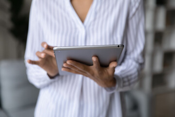 Crop close up of mixed race female hold modern tablet work online on device at home. African American woman use pad gadget browse surf wireless internet web. Technology, electronics concept.