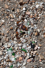 Shards of broken bottles among stones on the road. Environmental pollution.