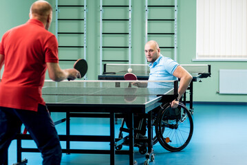 Fototapeta na wymiar Adult disabled man in a wheelchair play at table tennis with his coach