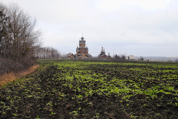 Fototapeta na wymiar The wooden church of the All Saints Skete behind a green field in autumn