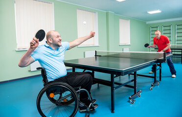 Adult disabled man in a wheelchair play at table tennis with his coach