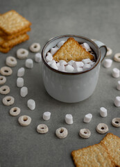 a gray ceramic mug, marshmallows and cookies in a mug, a pattern of marshmallows and cereal is lined around; morning composition for breakfast in a light key