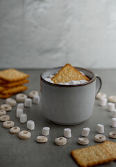 a gray ceramic mug, marshmallows and cookies in a mug, a pattern of marshmallows and cereal is lined around; morning composition for breakfast in a light key