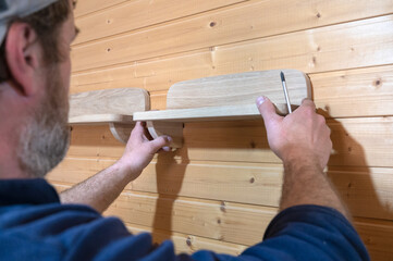 hands of a master carpenter attach a wooden shelf to the wall. Production of handmade furniture to...