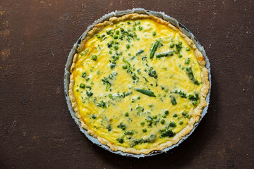 Quiche pie with spinach, green peas, asparagus beans and egg topping in a baking dish on a brown concrete background. French cuisine. Savory pastry recipes