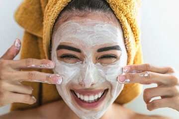 Young woman applying cream on face - Happy girl having skin care spa day at home - Healthy beauty...