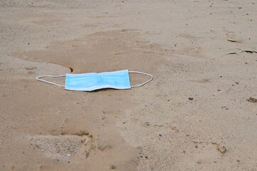 used disposable medical mask lies on the sand. Problems of environmental pollution and medical...