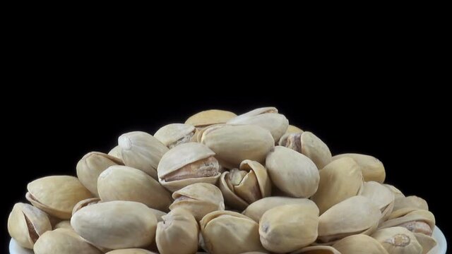 A heap of pistachio nuts rotates on a black background. 