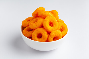 Popular Ready to eat crunchy and puffed snacks ring tangy orange color in a white ceramic bowl. Top view, Side lit,