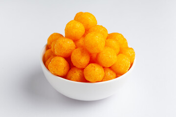 Close up of Cheese Potato Puff Ball Snacks, tangy orange color, Popular Ready to eat crunchy and puffed snacks,  salty in white ceramic bowl over white background