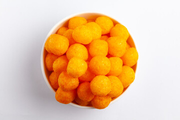 Close up of Cheese Potato Puff Ball Snacks, tangy orange color, Popular Ready to eat crunchy and puffed snacks,  salty in white ceramic bowl over white background