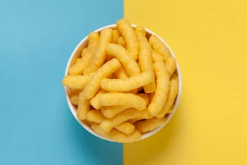 Foto op Aluminium Close up of Cheese Potato Puff Snacks sticks, Popular Ready to eat crunchy and puffed snacks sticks  cheesy salty pale-yellow color over Blue-Yellow background © Prashant ZI
