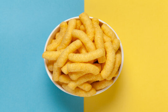 Close up of Cheese Potato Puff Snacks sticks, Popular Ready to eat crunchy and puffed snacks sticks  cheesy salty pale-yellow color over Blue-Yellow background