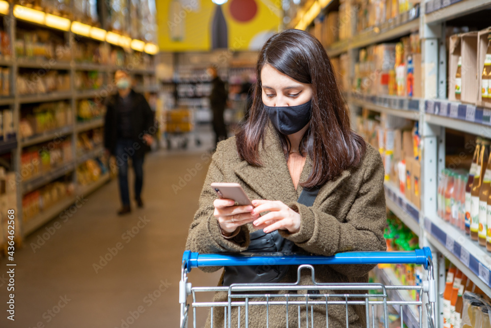 Wall mural woman with phone checking shopping list app in grocery store