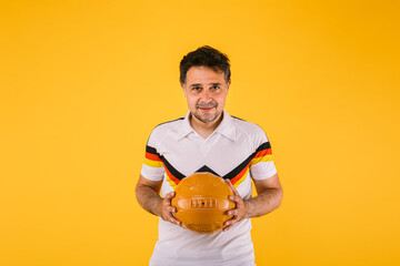 Soccer fan wearing a white t-shirt with black, red and yellow stripes, holds a retro ball in his hands
