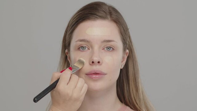 Makeup artist or stylist applies foundation to the face of the female model. Visagiste  applying cosmetic foundation base on a face. Professional makeup. Tutorial makeup.