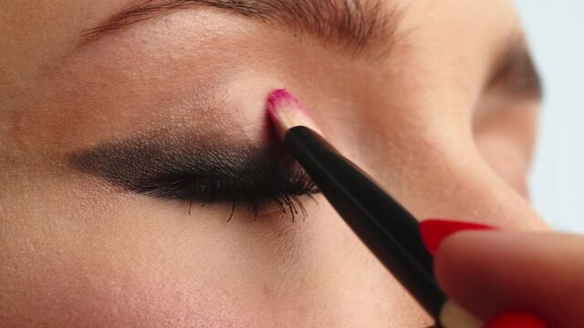 Make-up artist applies  pink color makeup to the upper eyelid, close-up.  Makeup artist applies a bright eye shadow with a makeup brush. Slow motion cinematic shoot.