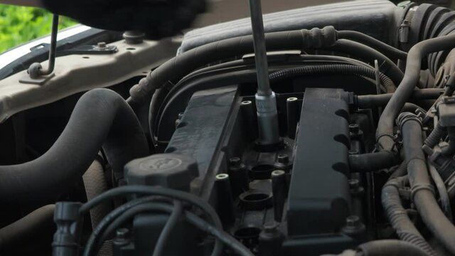 a man installs spark plugs on a dusty car engine. car repair. scheduled maintenance