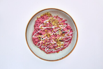 Salad of boiled beetroot with garlic, prunes, mayonnaise, sprinkled with crushed walnuts, decorated with strips of mayonnaise in a white round plate on a white background.