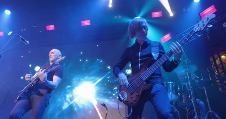 Live concert. Performance of a pop group, music band on stage. Stage light and bright flashes. Vocalist, guitarist. Slow motion