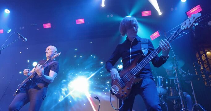 Live concert. Performance of a pop group, music band on stage. Stage light and bright flashes. Vocalist, guitarist. Slow motion