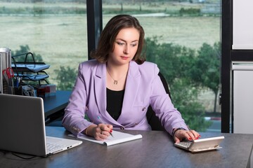 Business woman accountant in purple suit in the office uses a calculator and writes data in a...