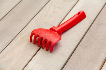 Toy kids plastic red rake on wooden bench background. Forgotten or lost toy in the playground