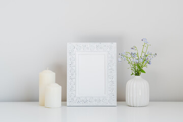Vertical photo frame mockup, candles, vase with fresh flowers on white table. Elegant, minimal home interior design. Still life.