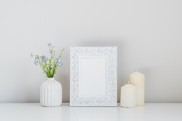 Photo frame mockup, candles, vase with spring flowers on white background.