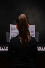 Fototapeta na wymiar Rear view of young girl practicing the piano in solemn dark atmosphere. Practicing PIANO CONCEPT.