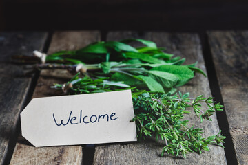 Fresh herbs and spices on wooden table welcome label