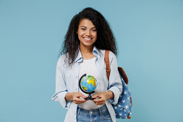 Young smiling african american girl teen geography student wear denim clothes backpack hold in hands Earth world globe isolated on blue background Education in high school university college concept.